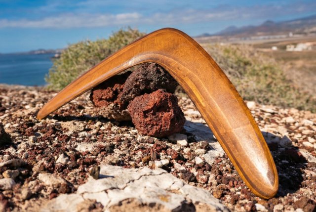 Tamsus medinis bumerangas, balansuojantis ant akmenų gamtoje.