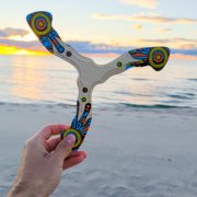 Rankų darbo bumerangas „Šamanas“ laikomas rankoje pajūryje leidžiantis saulei.
