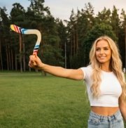 Mergina-laiko-bumeranga-Vejas-gamtoje Jauna moteris ruošiasi mesti bumerangą „Vėjas“ parke, miško fone.